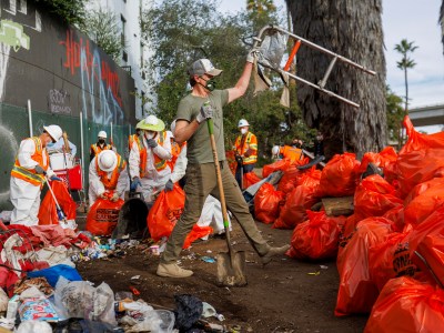 Surrounded by workers in hazmat suits and bright orange waste bags, Gov. Gavin Newsom helps clear a homeless encampment in San Diego.