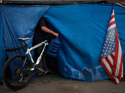 A faded American flag hangs outside of a pitched tent on the Santa Ana River trail as an unhoused person walks into the tent in Anaheim on Jan. 22, 2018. Photo by Jae C. Hong, AP Photo