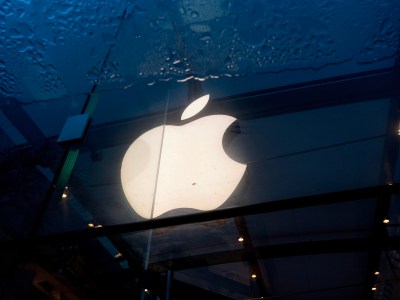 A bright and lit Apple logo is reflected in a puddle of water.