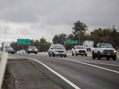 A group of cars driving northbound on a highway with overcast in the sky.