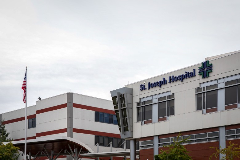 The white and red facade of a hospital is visible. On the left, an American flag rests on a flagpole. On the facade, the words, "St. Joseph Hospital" are visible.