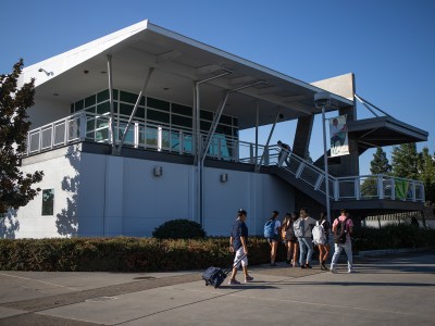 A wide view of a group of students walking by a two-story building at a college campus.