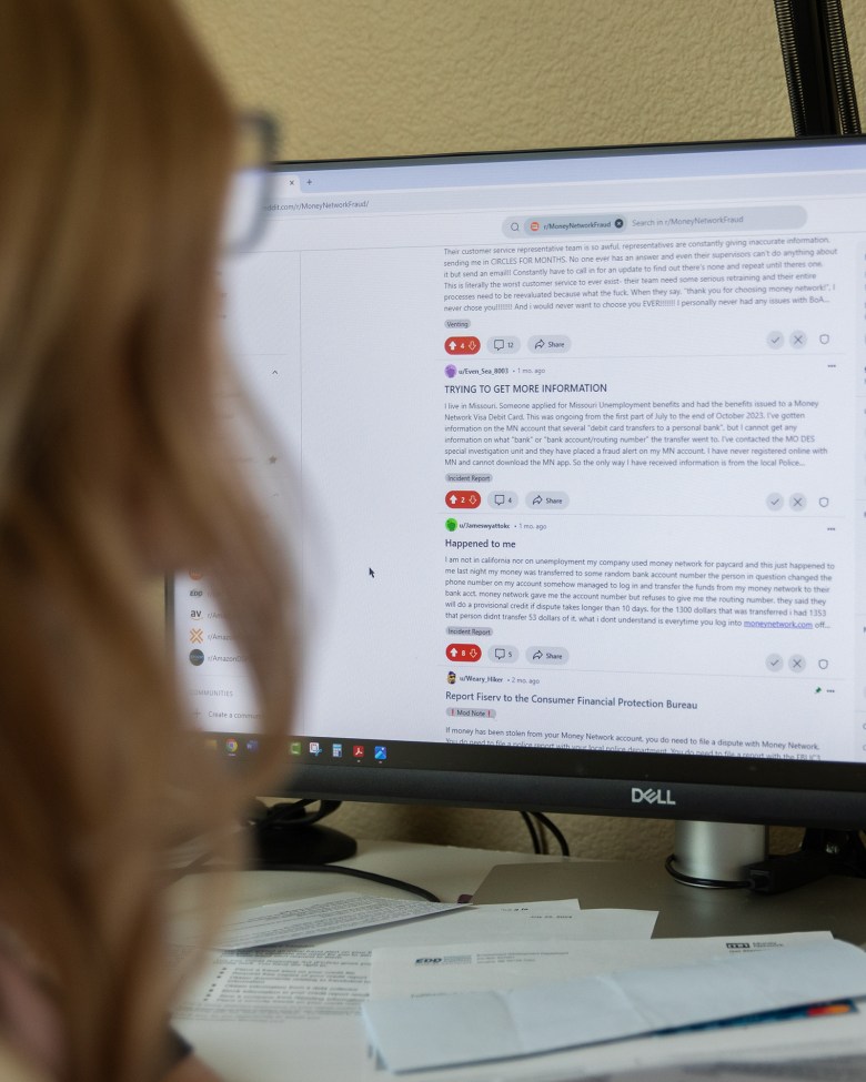 A computer screen showing a subreddit with various posts by users asking questions or sharing their experiences with money fraud and identity theft. A person with blond hair can be seen in the foreground looking towards the screen.