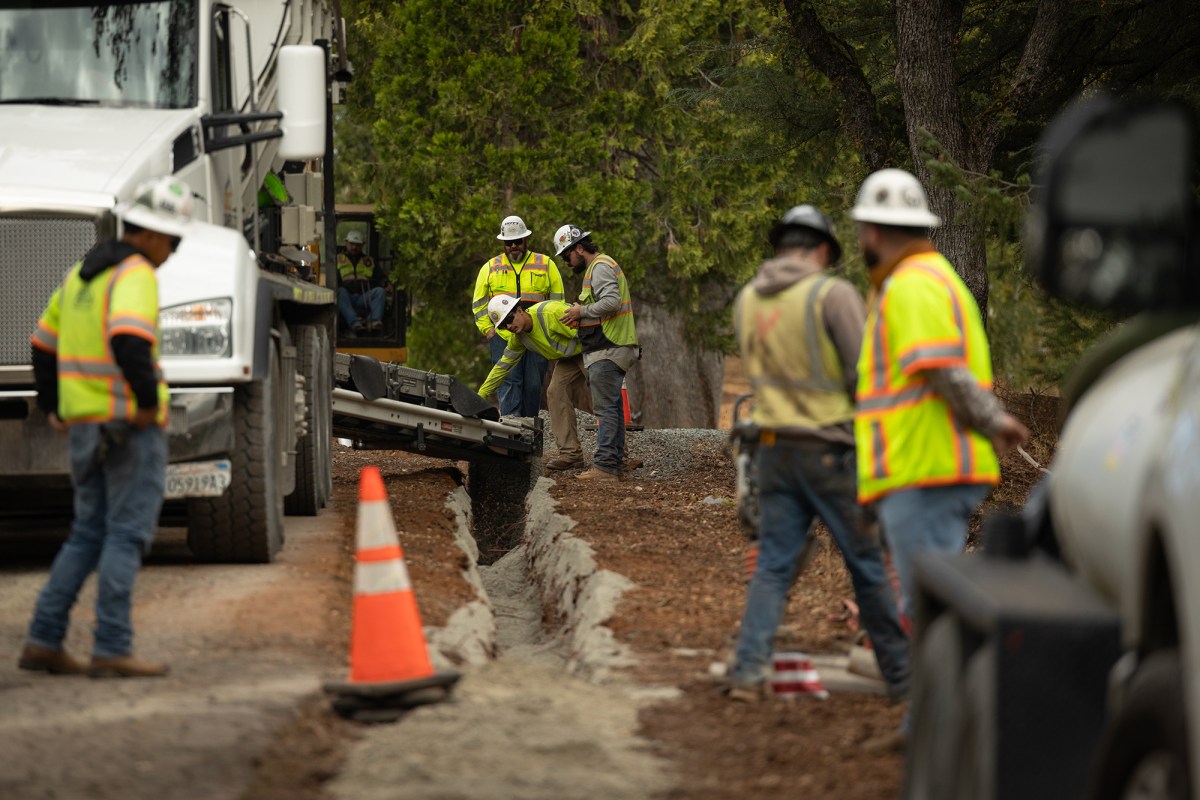 People wearing yellow and orange safety vest and white hard hats work on a trench to lay underground electric cables.