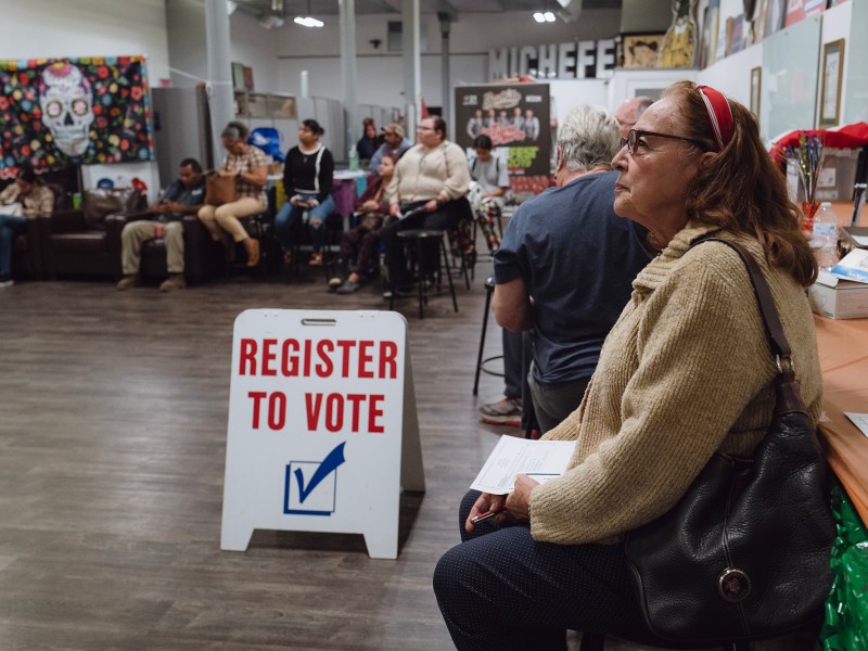 Rosalinda Avitia, 73, listens to organizers as they review voter registration information in Tulare on Nov. 1, 2023. Photo by Zaydee Sanchez for CalMatters