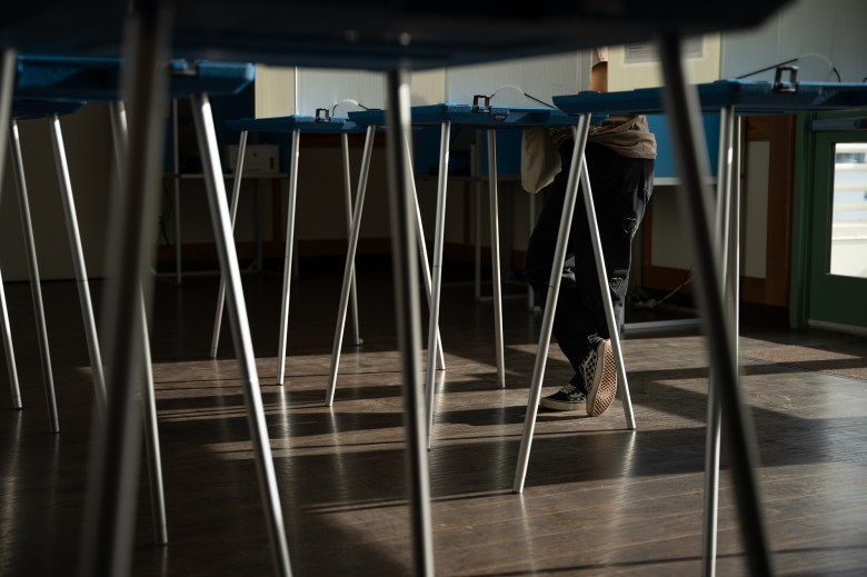 A close-up view of a person's checkered pattern shoes as they lean over a voting booth at a vote center.