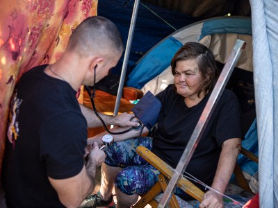 Physician's assistant Brett Feldman checks his patient, Carla Bolen’s, blood pressure while in her encampment at the Figueroa St. Viaduct above Highway 110 in Elysian Valley Park in Los Angeles on Nov. 18, 2022.Photo by Larry Valenzuela for CalMatters