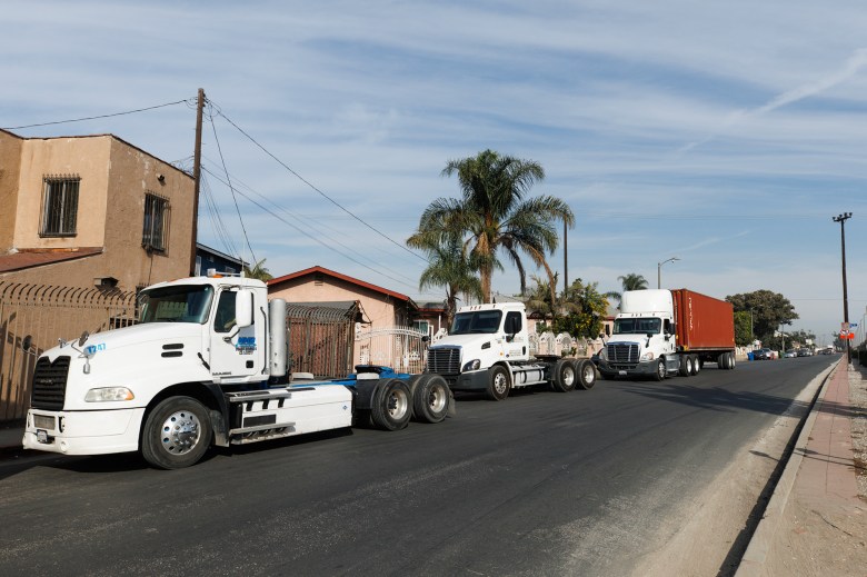 A wide-view of three commercial trucks parked on the side of a streets with houses in the background.