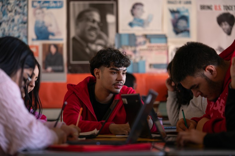 A close-up view of students sitting at desks and facing each other as they work on a project.