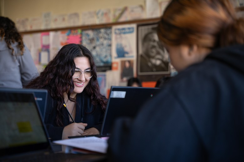 A close-up view of a student sitting at desks and looking at their laptops as they write on a piece of paper.