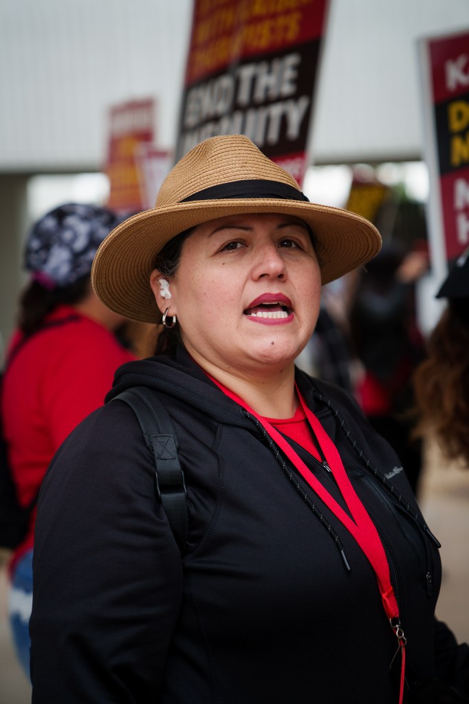 A portrait of a woman wearing a fedora hate, black sweater and red shirt during a strike.