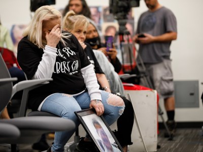 A person sits in a chair looks downwards while placing their right hand on their forehead as they hold a frame of their loved one with their left hand.