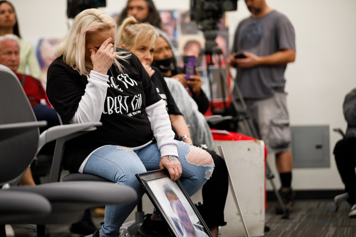 A person sits in a chair looks downwards while placing their right hand on their forehead as they hold a frame of their loved one with their left hand.